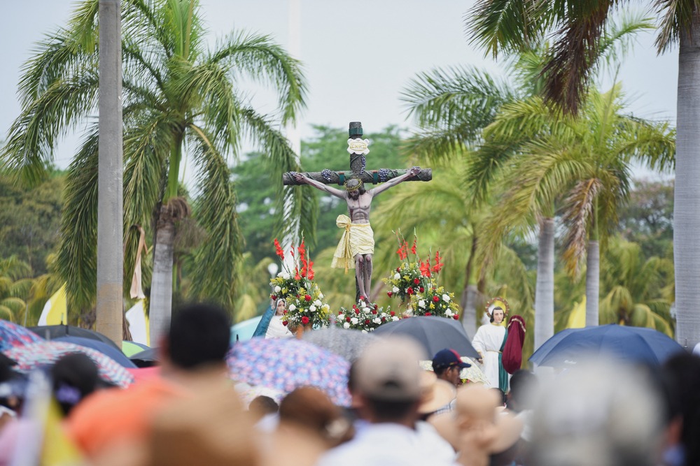 Crucifix on flowered float, framed by grove of palm trees.