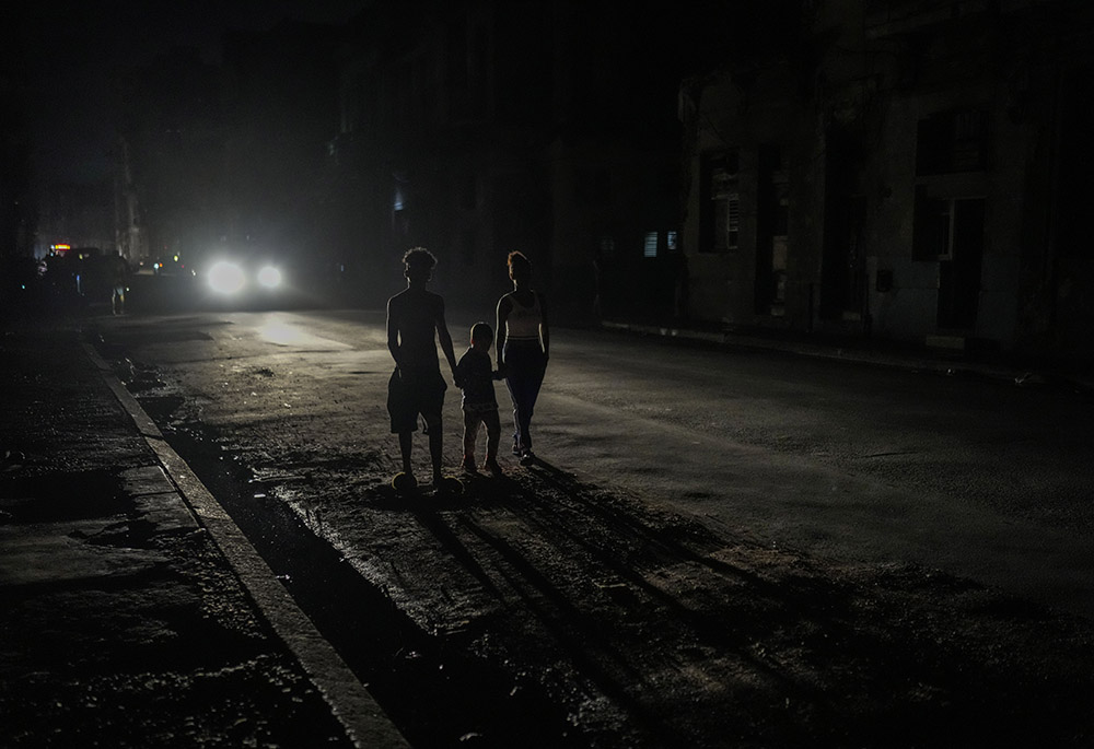 Residents are illuminated by the headlights of a car during a blackout after a major power plant failed Oct. 18 in Havana, Cuba. (AP photo/Ramon Espinosa, file)