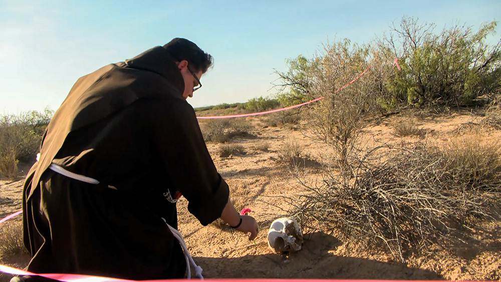 Franciscan Br. Maikel Gomez Perez kneels to pray and place a carnation by a skull left at a site of human remains in the desert in Santa Teresa, New Mexico. (KTSM/Jesus Baltazar)     