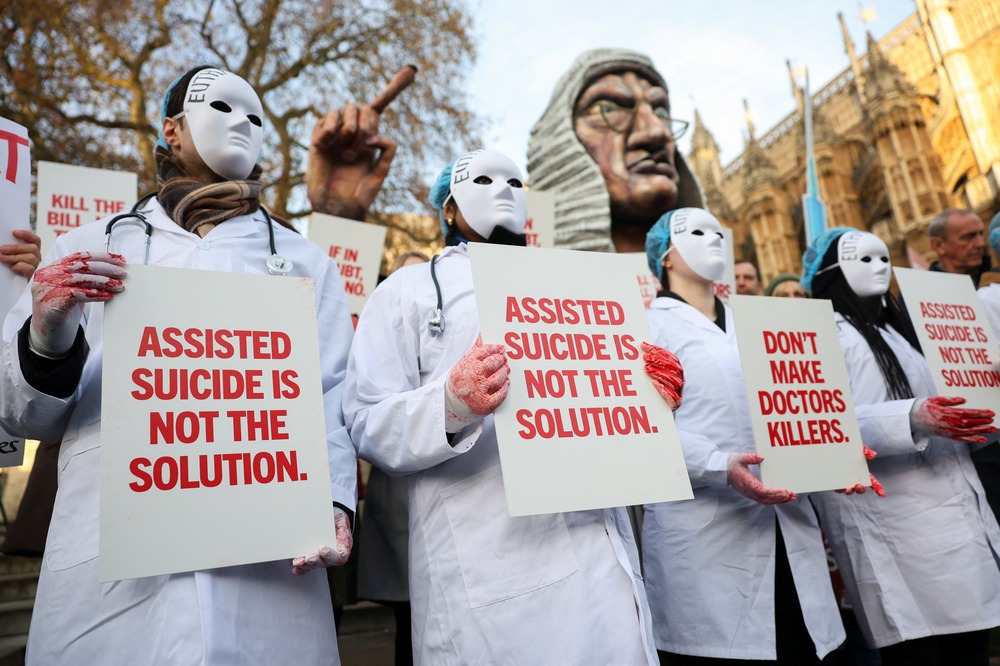 Masked protesters wear white medical coats and hold signs reading "Assisted suicide is not the solution."