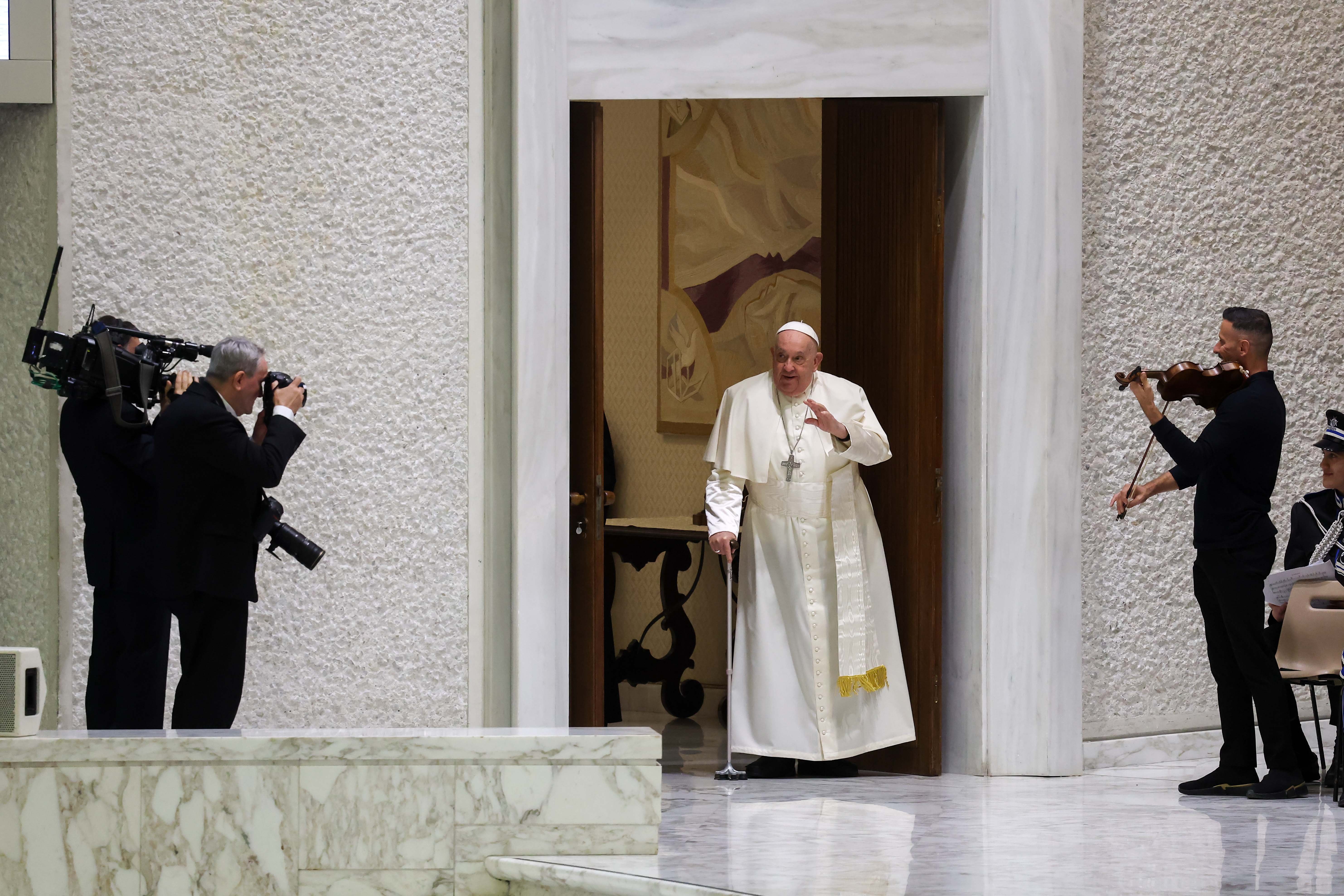 The pope enters room alone using cane.