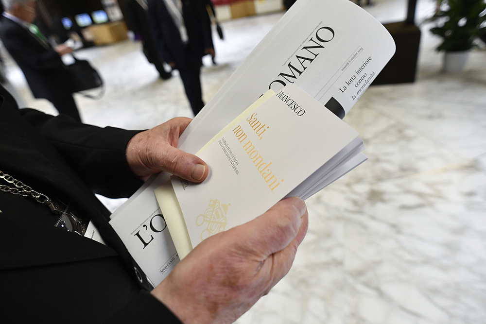 A member of the assembly of the Synod of Bishops carries a copy of the Vatican newspaper and the Italian edition of Pope Francis' book, "Holy, Not Worldly: God's Grace Saves Us From Interior Corruption," in the Vatican's Paul VI Audience Hall Oct. 6, 2023. (CNS/Vatican Media)