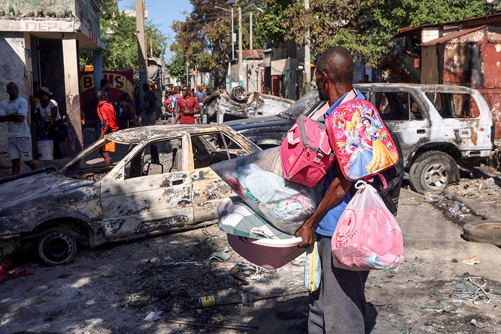 A man carrying his belongings observes the wreckage of vehicles burned by armed gangs as he flees the Poste Marchand suburb in Port-au-Prince, Haiti, Dec. 9, 2024. (OSV News/Reuters/Ralph Tedy Erol)