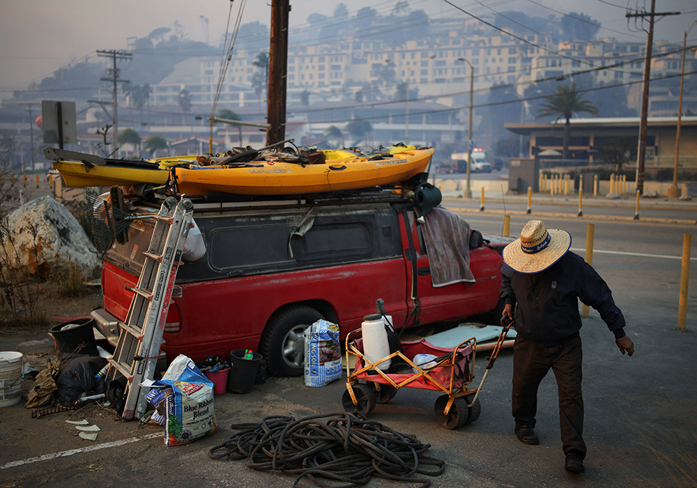 A man collects water along the Pacific Coast Highway, as powerful winds fueling devastating wildfires in the Los Angeles area force people to evacuate, in the Pacific Palisades neighborhood on the west side of LA on Jan. 8. Several Catholic parishes opened their doors to families evacuated from their homes as wind-driven fires continued to burn through parts of Los Angeles County Jan. 8. (OSV News/Reuters/Daniel Cole)