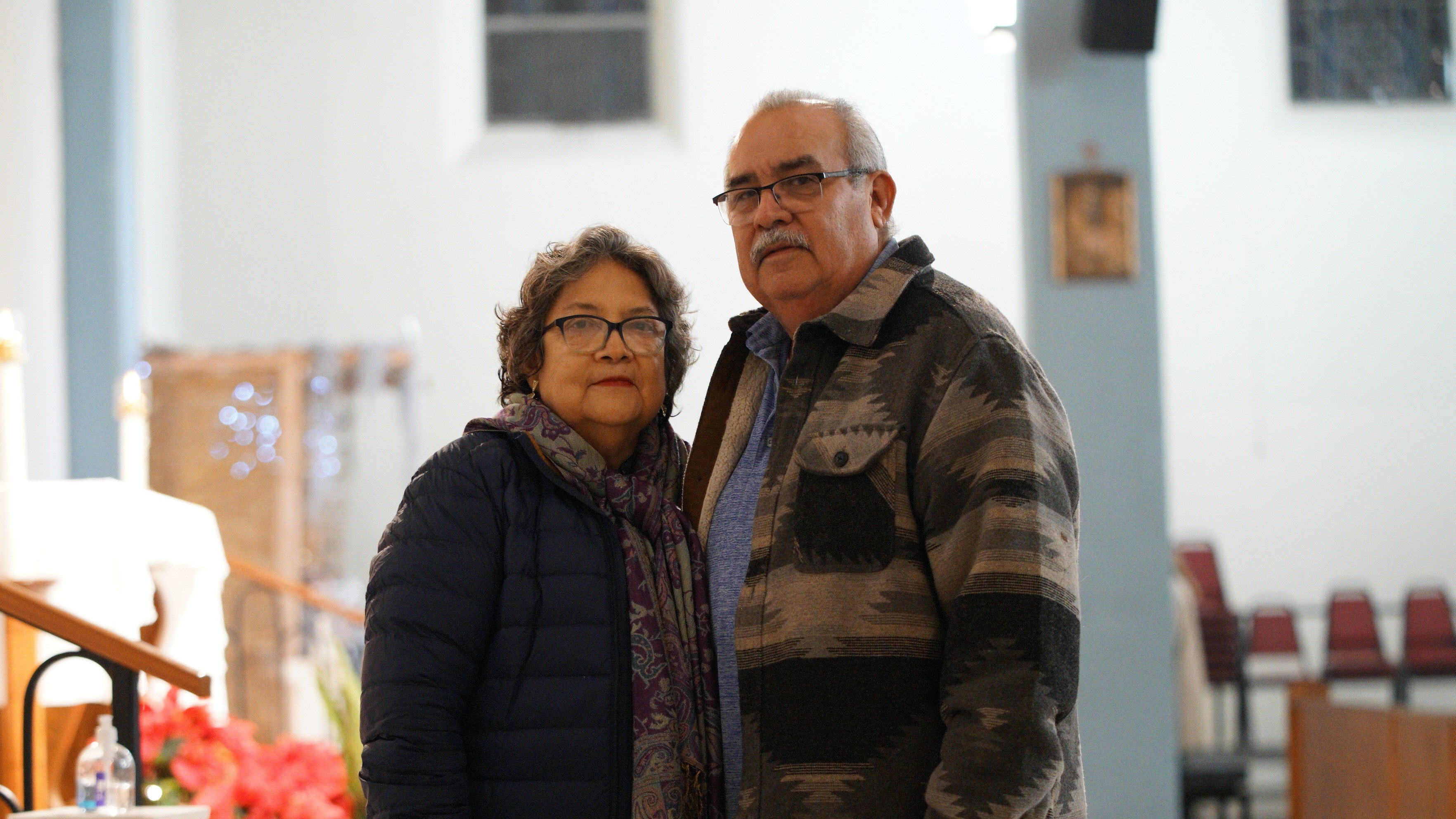 Older couple standing side by side, arms around each other.