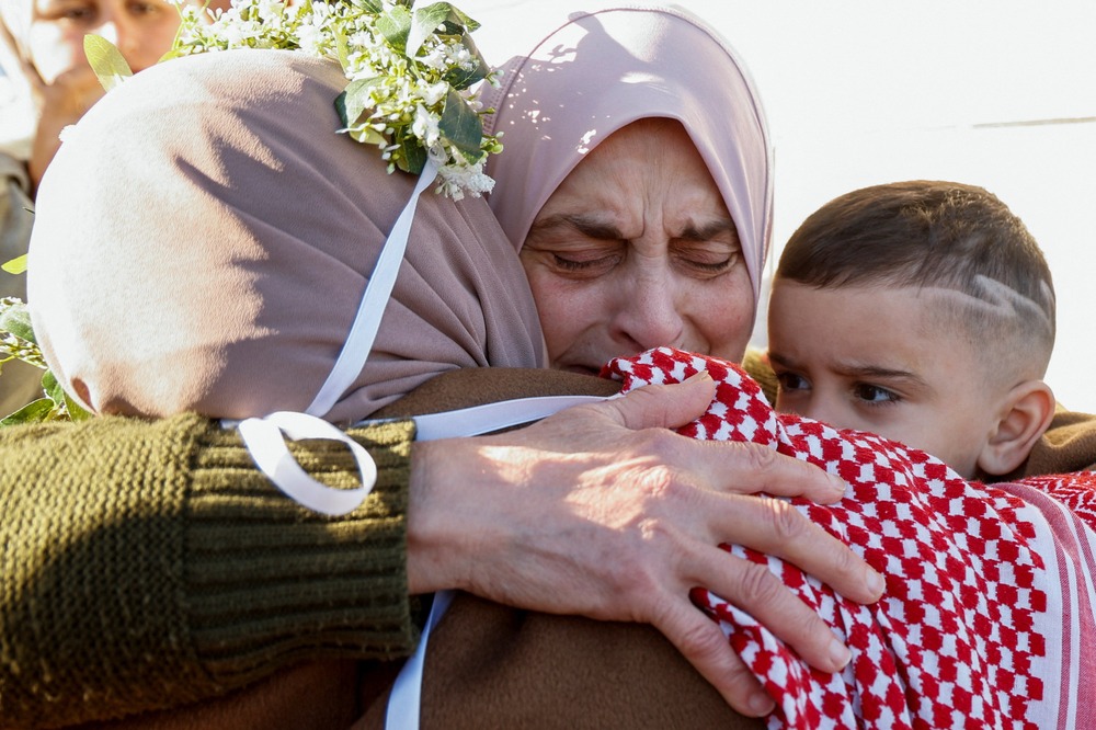 Woman's face crinkles with emotion as she embrace other woman and young boy.