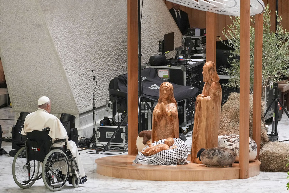 Francis in wheelchair pictured from behind regarding the nativity scene. 