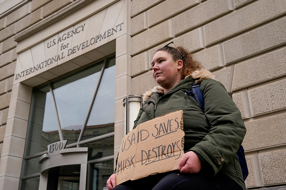 A woman holds a placard outside the U.S. Agency for International Development building in Washington as it sits closed to employees Feb. 3, 2025, after a memo was issued advising agency personnel to work remotely. (OSV News/Reuters/Kent Nishimura)