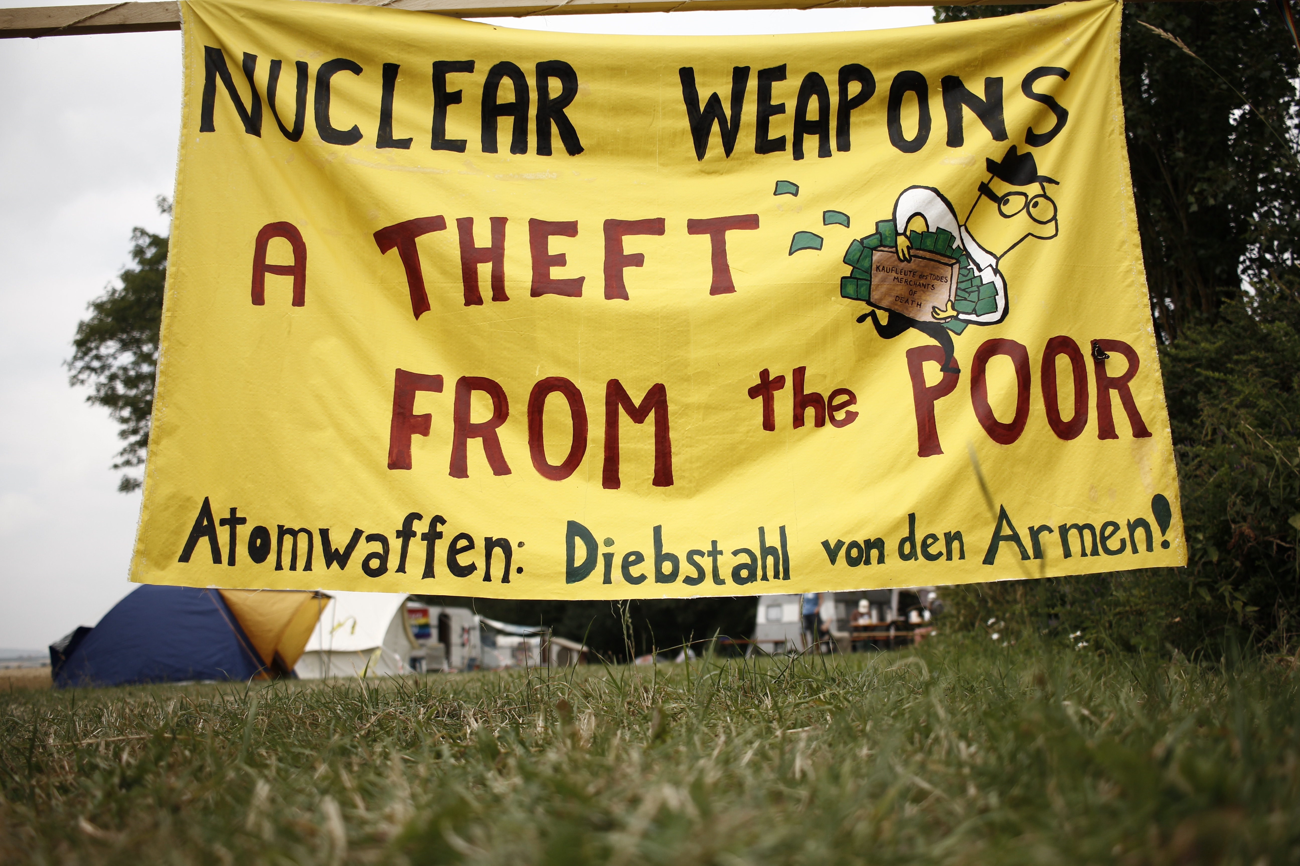 A yellow painted banner from Crane’s protest reads "NUCLEAR WEAPONS: A THEFT FROM THE POOR" in red text.