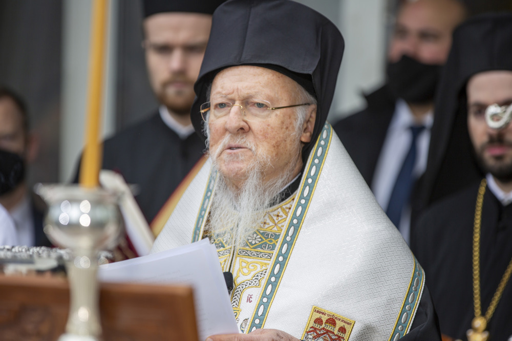 Patriarch in vestments standing at lectern reading from written speech.