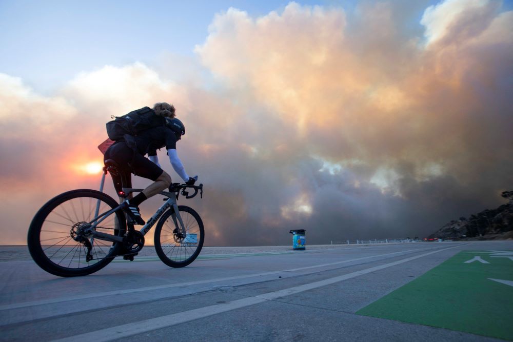 Man rides bike, with fire and windstorm in background