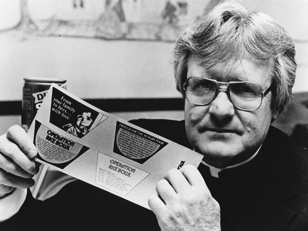 Msgr. Robert Coll, one of the founders of Operation Rice Bowl in the Diocese of Allentown, Pennsylvania, shows collection can labels for the national campaign in 1979. (CNS/Paul Cullen)