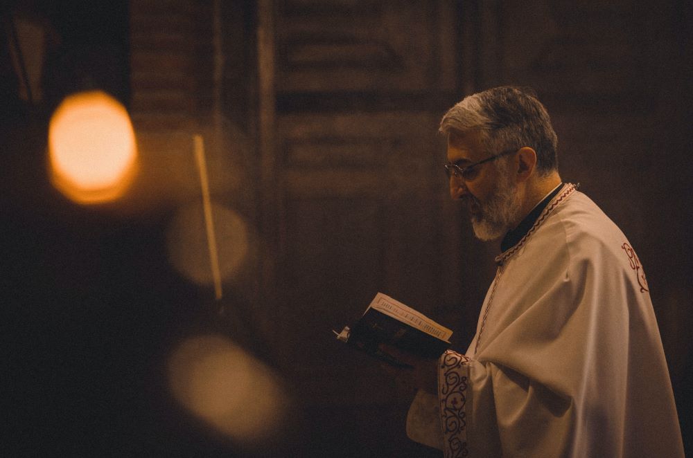 Picture of a priest holding a book (Unsplash/Tamara Govedarov)