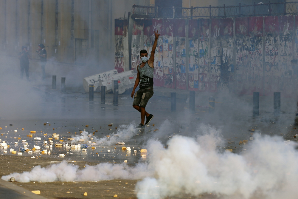 An anti-government protester flashes the victory sign amid tear gas fired by riot police during a protest marking the first anniversary Aug. 4 of the massive blast at Beirut's port, near Parliament Square in Beirut, Lebanon. (AP/Bilal Hussein)