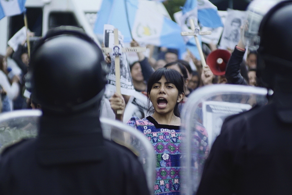 Backs of riot police seen, faces of people protesting