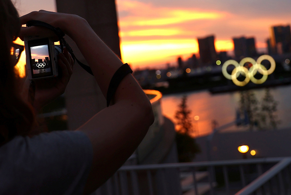 A person photographs the Olympic Rings in front of the skyline during sunset July 20 in Tokyo, three days ahead of the official opening of the 2020 Olympic Games. (CNS/Reuters/Kai Pfaffenbach)