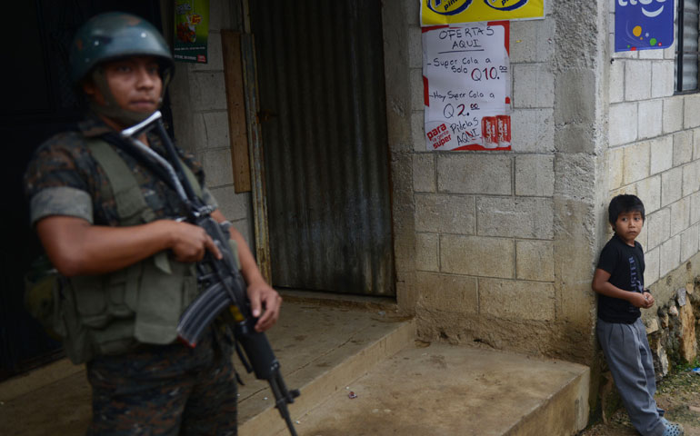 A child looks at a soldier standing guard at a crime scene where 11 people were killed by alleged members of a gang in San José Nacahuil, Guatemala, Sept. 8, 2013. (AFP/Getty Images/Johan Ordonez)