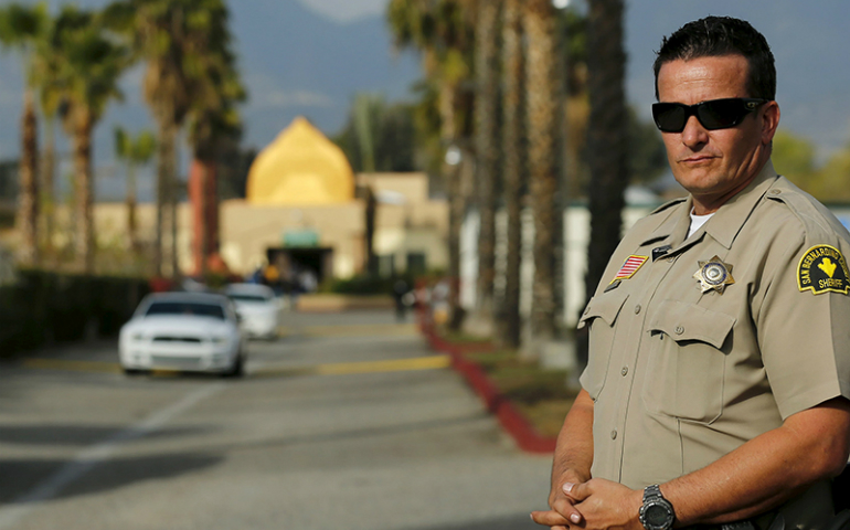 A police officer stands watch on Dec. 4, 2015, as people leave Friday prayers at the Dar Al Uloom Al Islamiyah-Amer mosque in San Bernardino, Calif., where shooting suspect Syed Rizwan Farook was seen two to three times a week at lunchtime. (Photo courtesy of REUTERS/Mike Blake)