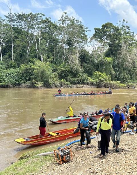 Small boats pull to river shore, as people step onto land.