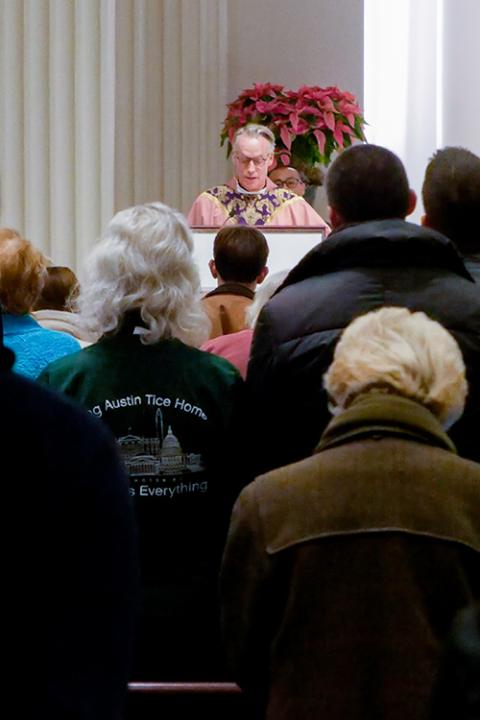 As Debra Tice listens, Jesuit Fr. Jack Dennis reads the Gospel at Mass Dec. 15 at Holy Trinity Church in Washington. (NCR photo/Anthony Peltier)