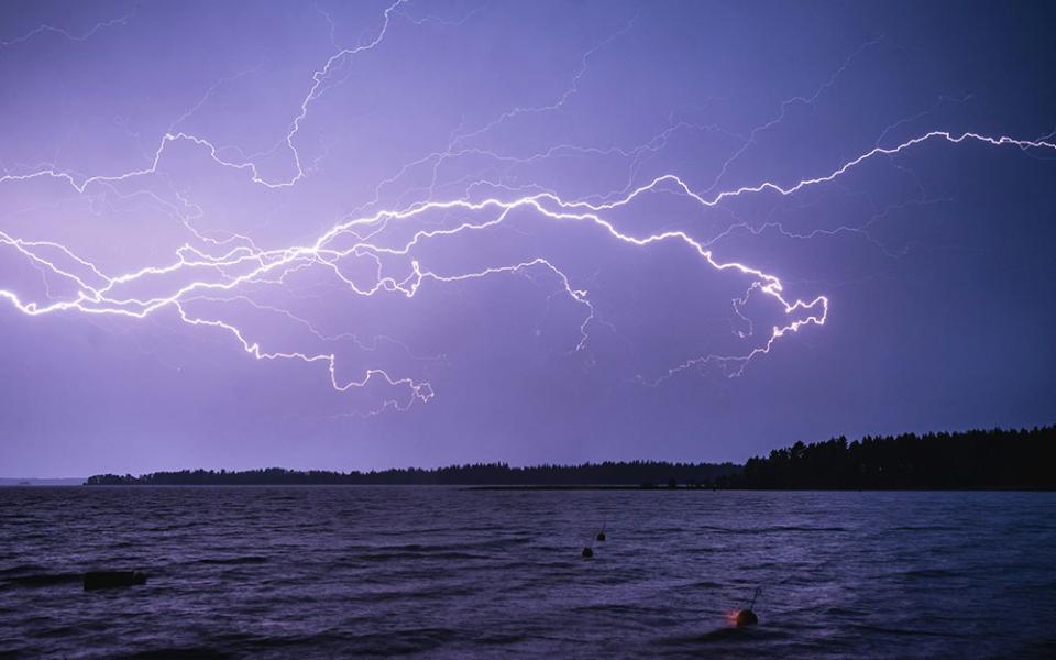 In this photo illustration lightning strikes across a night sky, lighting up a body of water below. (Unsplash/Niilo Isotalo)