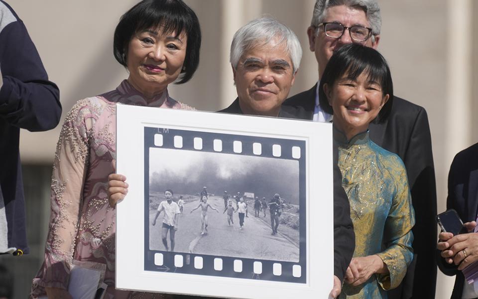 Pulitzer Prize-winning photographer Nick Ut, center, flanked by Kim Phúc, left, holds the "Napalm Girl", his Pulitzer Prize winning photo, as they wait to meet with Pope Francis during the weekly general audience in St. Peter's Square at The Vatican, on May 11, 2022. (AP photo/Gregorio Borgia, file)