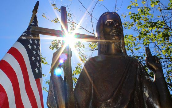 Sun shines through a statue of Christ on a grave marker alongside an American flag June 7, 2018, at St. Mary Catholic Cemetery in Appleton, Wisconsin. (CNS/Bradley Birkholz)