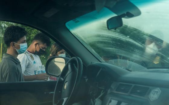 Migrants from Central America in Penitas, Texas, are seen next to a car as they are processed by a U.S. Border Patrol agent after crossing the Rio Grande July 8. (CNS photo/Go Nakamura, Reuters)