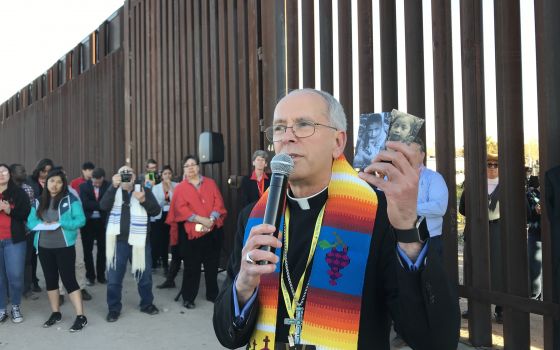 Bishop Mark J. Seitz of El Paso, Texas, is seen Feb. 26, 2019, at the U.S.-Mexico border wall holding photos of two migrant children who died in U.S. custody. (CNS photo/David Agren)