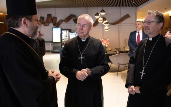 Three older white men clerics chat in an lobby