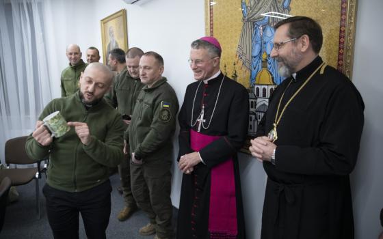 Archbishop Broglio speaks with men dressed in green military attire as another archbishop looks on