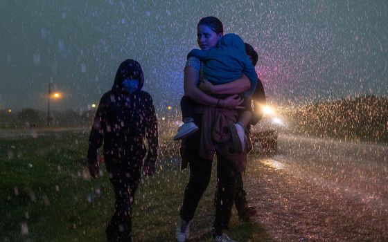 A mother from Central America and her three children are followed by a Texas Highway Patrol officer in La Joya, Texas, May 19, 2021, as they look for cover during a heavy rainfall after crossing the Rio Grande into the United States from Mexico. (CNS)