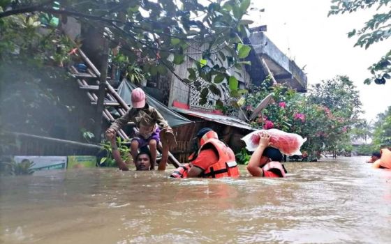 A man carries a boy on his shoulder April 10, 2022, as they walk on a flooded road after Tropical Storm Megi hit Capiz, Philippines. (CNS/Reuters/Philippine Coast Guard Handout)