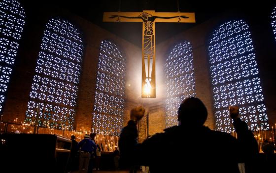 A person in shadow raises both fists below an illuminated crucifix