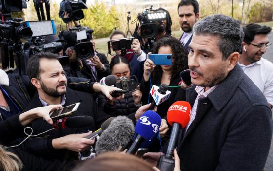 People with microphones and professional cameras crowd around a brown man