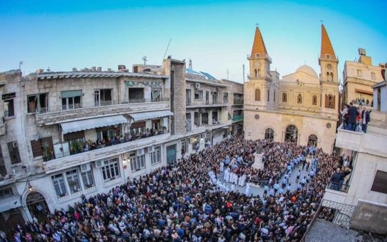 A crowd gathers in a plaza in front of a steepled church. Other people watch from apartment balconies.