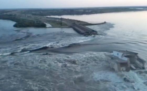 Water flows over banks and between two broken parts of a concrete dam