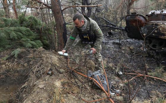 A Ukrainian soldier picks up unexploded parts of a cluster bomb left after Russia's invasion near the village of Motyzhyn, Ukraine, April 10, 2022. (OSV News/Reuters/Mykola Tymchenko)