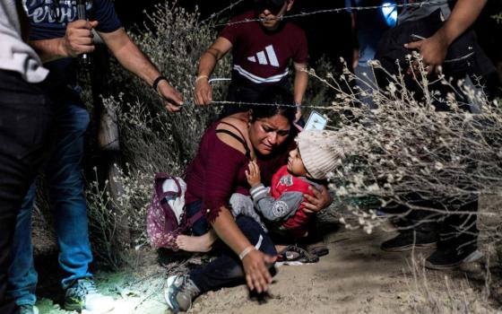 Asylum-seeking migrants' families go under a barbed wire fence while being escorted by a local church group to the location where they turn themselves in to the U.S. Border Patrol, after crossing the Rio Grande river into the United States from Mexico, in Roma, Texas, April 16, 2021. Catholic and human rights organizations react to July 2023 reports that Texas authorities are employing inhumane tactics against migrants and asylum seekers along the Rio Grande. (OSV News photo/Go Nakamura, Reuters)