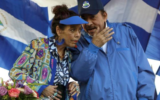 A man wearing a light blue coat talks into the ear of a woman wearing a similar colored visor