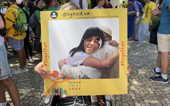 A young man puts his head through a cutout frame to take a photo "hugging" Pope Francis at the Synod of Bishops' booth in a park in Lisbon, Portugal, during World Youth Day Aug. 3. (CNS/Courtesy of the Synod Secretariat)