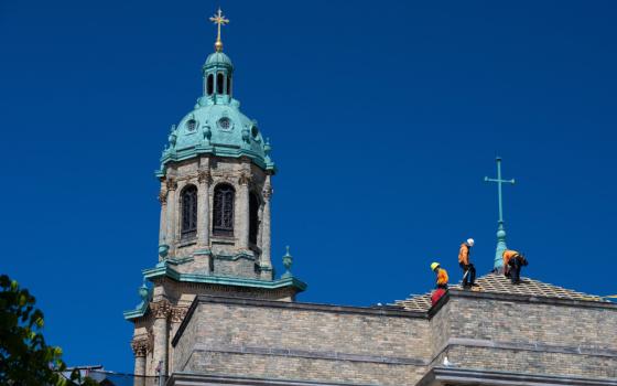 Construction workers stand on the roof of a church with a coppery green dome and cross