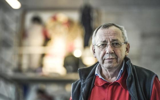 An older white man wearing glasses, a vest, and a collared shirt looks at the camera