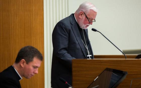 Bishop speaks at microphone. Another cleric listens.