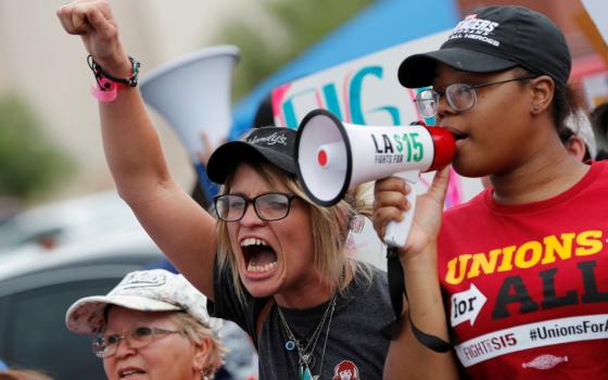 A crowd of people including a person holding a megaphone and a person with a fist raised gather