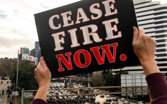 A protester holds a sign calling for a cease-fire to the Israel-Hamas war as others block Interstate 5 northbound on Jan. 6 in downtown Seattle. (AP/Lindsey Wasson)