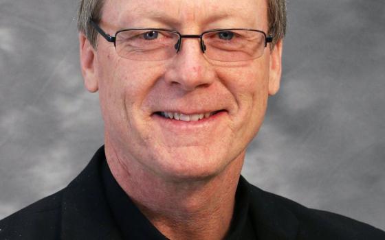 An older white man wearing glasses and a clerical collar smiles at the camera