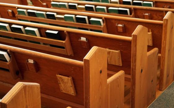 Empty church pews are visible from behind. There are hymnals and books in racks.