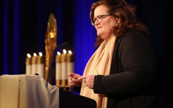 Teresa Pitt Green stands at lectern, speaking with candles in background.