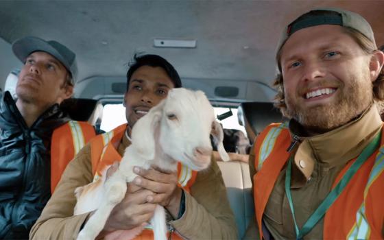 Three men, center man holds goat